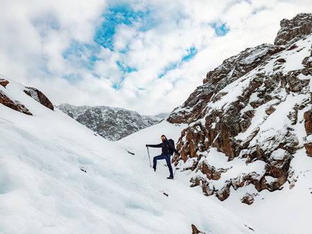A male hiker high up in the mountains in winter. Bearded traveler with a backpack standing on a snowy slope. Hiking in the winter mountainsの写真素材