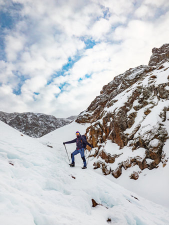 A male hiker high up in the mountains in winter. Bearded traveler with a backpack standing on a snowy slope. Hiking in the winter mountainsの写真素材