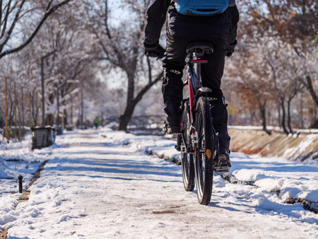 A rear view of a cyclist riding on an icy sidewalk on a winter day. Active lifestyle in winterの写真素材