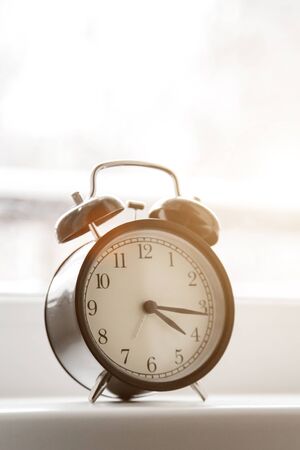 An alarm clock stands on a window in the morning light.
