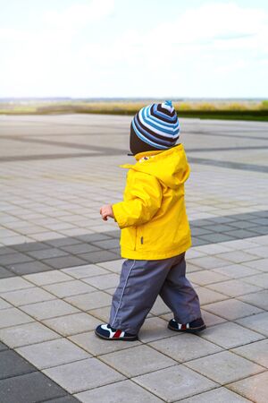 A small child in a yellow jacket walks along the alley. Walk and children's health.の写真素材