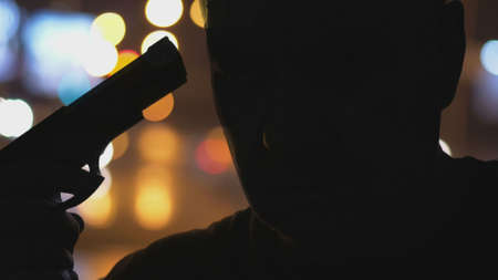 Silhouette Of Serious Male Holding Pistol And Preparing To Kill Himself Suicideの写真素材