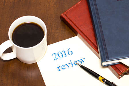 The 2016 review the text on the sheet of paper next to a Cup of coffee, pen, business diary on wooden tableの写真素材