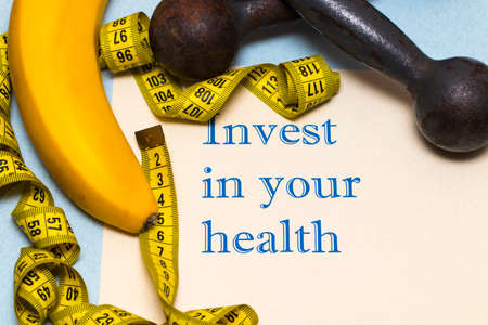 Invest in your health - the inscription on the sheet of paper with dumbbells, banana and rouletteの写真素材