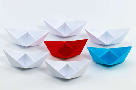 Leadership concept with red paper ship leading among white.