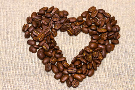 heart made with coffee beans stacked against burlap canvas.の写真素材