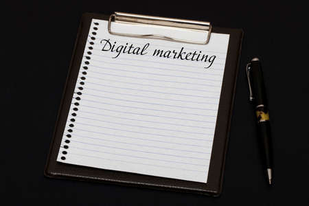 Top view of clipboard and white sheet written with Digital marketing on black background. Business Concept.の写真素材