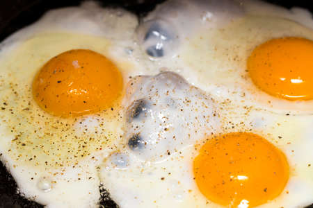 Fried eggs in a frying pan  for breakfast on a black background.