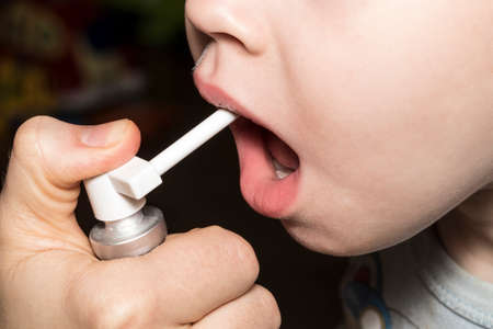 Baby getting medicine through oral spray for sore throat. Mother or doctor treats her child's...