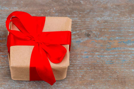 Gift box present with red bow ribbon and brown krafts wrapping paper on  wooden background,the view...
