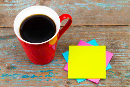 Cup of coffee and a  sticky notes with empty space for a text on wooden background.の写真素材