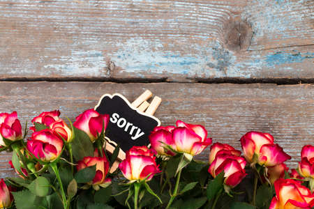 Text: sorry. Background with roses and chalkboard on wooden table. Top view with copy space.