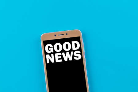 Good news inscription on phone screen. Golden phone on a blue background.の写真素材