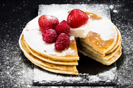 Pancakes with berries and sugar on dark background.