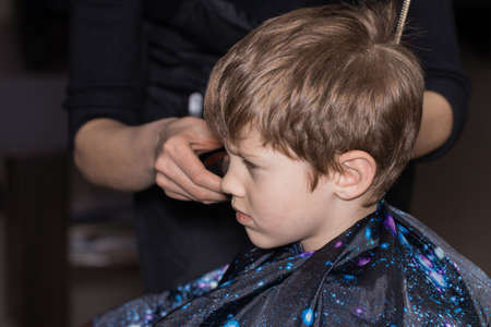 Side view of cute little boy getting haircut by hairdresser at the barbershop.の写真素材