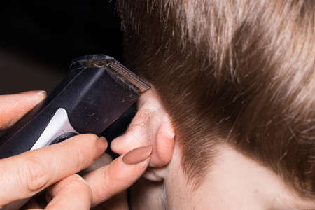 Side view of cute little boy getting haircut by hairdresser at the barbershop using comb and grooming scissors. Closeup.の写真素材