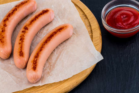 Grilled sausages with sauce ketchup on a wooden board.の写真素材