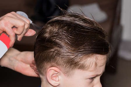 Side view of cute little boy getting haircut by hairdresser at the barbershop using comb and grooming scissors. Closeup.の写真素材