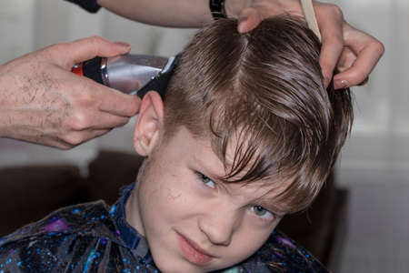 Side view of cute little boy getting haircut by hairdresser at the barbershop.の写真素材