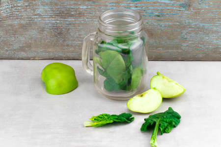 Green smoothie in glass jar with fresh organic green vegetables and fruits on grey background. Spring diet, healthy raw vegetarian, vegan concept, detox breakfast, alkaline clean eating. Copy space.の写真素材