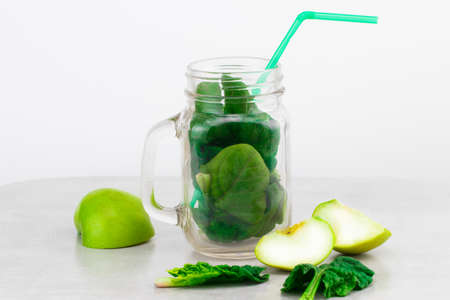 Green smoothie in glass jar with fresh organic green vegetables and fruits on grey background. Spring diet, healthy raw vegetarian, vegan concept, detox breakfast, alkaline clean eating. Copy space. top view.の写真素材