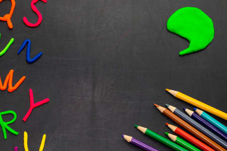 Black chalkboard with colorful pencils and letters, concept for education.