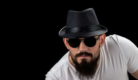 Silhouette of young confident handsome bearded man hipster in hat and sunglasses. Studio shot on dark background Image with free copy space.の写真素材