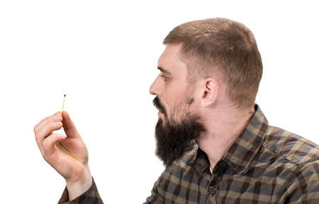 Close up portrait of attractive young serious or dangerous Caucasian man with burning match on his hand on white background. Brunette hipster in trendy spectacles posing indoors with fire in his hand.の写真素材