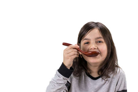 Portrait of  girl with wooden spoon in her mouth, isolated on white background with copy space.の写真素材