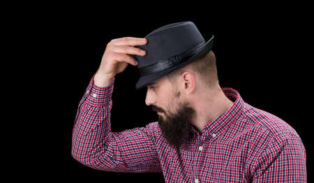 Pensive  bearded male dressed in a fleece shirt  and hat posing over black background.の写真素材