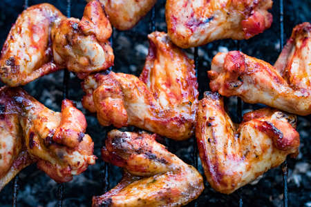 Spicy marinated chicken wings grilling on a summer barbecue with hot flames in a close up view.の写真素材