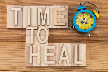 time to heal-  text in vintage letters on wooden blocks with alarm clock. Medicine concept.の写真素材