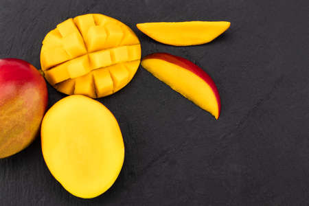 top view of ripe mango cut in half and diced on dark slate.の写真素材