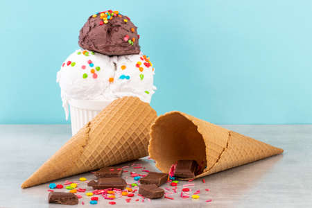 Plate of vanilla and chocolate ice cream scoops with sprinkles chocolate pieces and waffle cones on a blueの写真素材