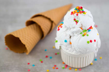 Plate of vanilla ice cream scoop with sprinkles and waffle cones.