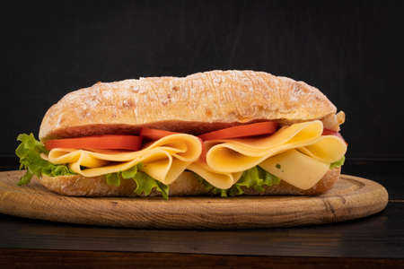Ciabatta sandwich with lettuce, prosciutto and  cheese on wooden board.