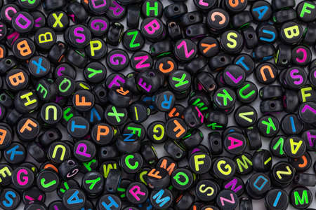Black plastic beads with colored letters placed randomly.