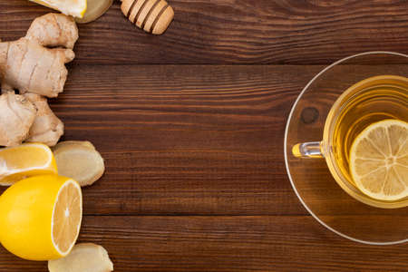 Cup of Ginger tea with lemon, honey and ginger root on a wooden
