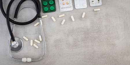 Stethoscope, pills, tablets and capsules on a gray background . Family healthcare, medicine and...