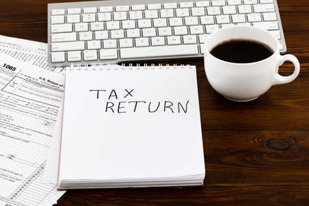 Tax Return written on paper note with tax form, and cup of coffee.