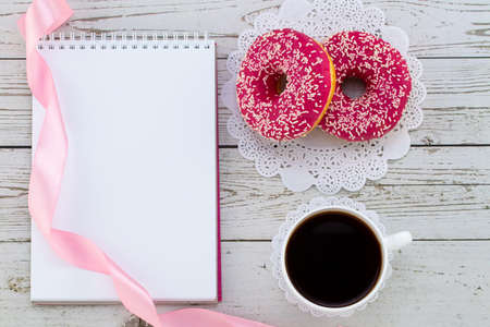 Donuts, coffee and empty notebook on a white wood background. Female working desk. Flat lay.の写真素材