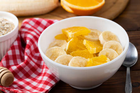 Bowl of oatmeal porridge with banana and orange  on wooden background, copy space.
