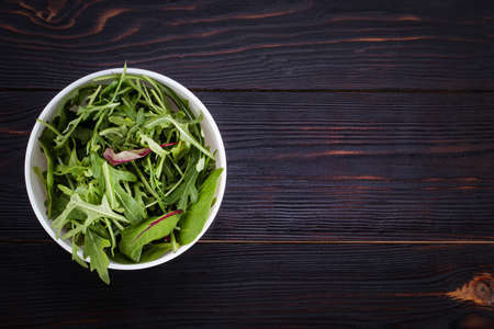 Fresh arugula in bowl, rucola salad on wooden rustic background. Copy space, top view.の写真素材