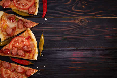 Slices of pizza with bavarian sausages, tomato and chili pepper on dark