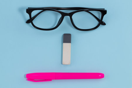 glasses eraser and pen on blue background education concept. abstract face.の写真素材