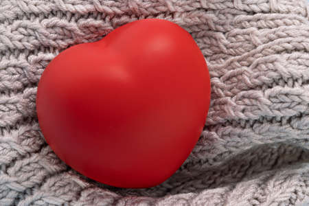 heart wrapped in a warm knitted scarf. Red heart on knitted texture background.の写真素材
