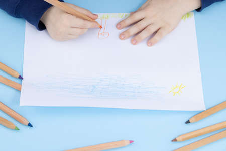 Close up of child's hands drawing at white paper within colorful pens and pencils.の写真素材