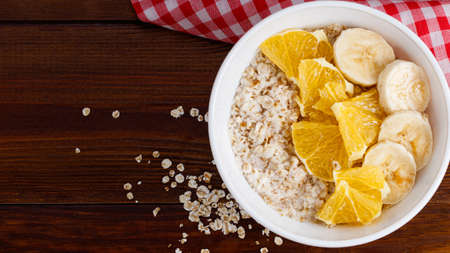 Bowl of oatmeal porridge with banana and orange on wooden background. Top view, copy space.の写真素材