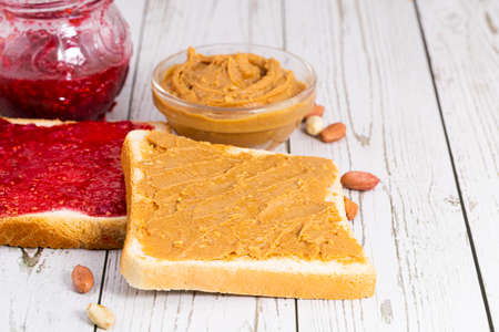 Toasts with peanut butter and berry jam on light wooden background.
