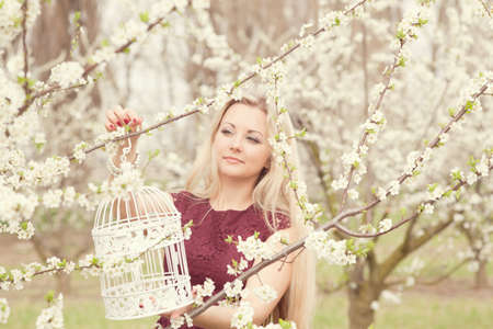Beautiful blonde girl in spring in a blossoming garden with a decorative cage